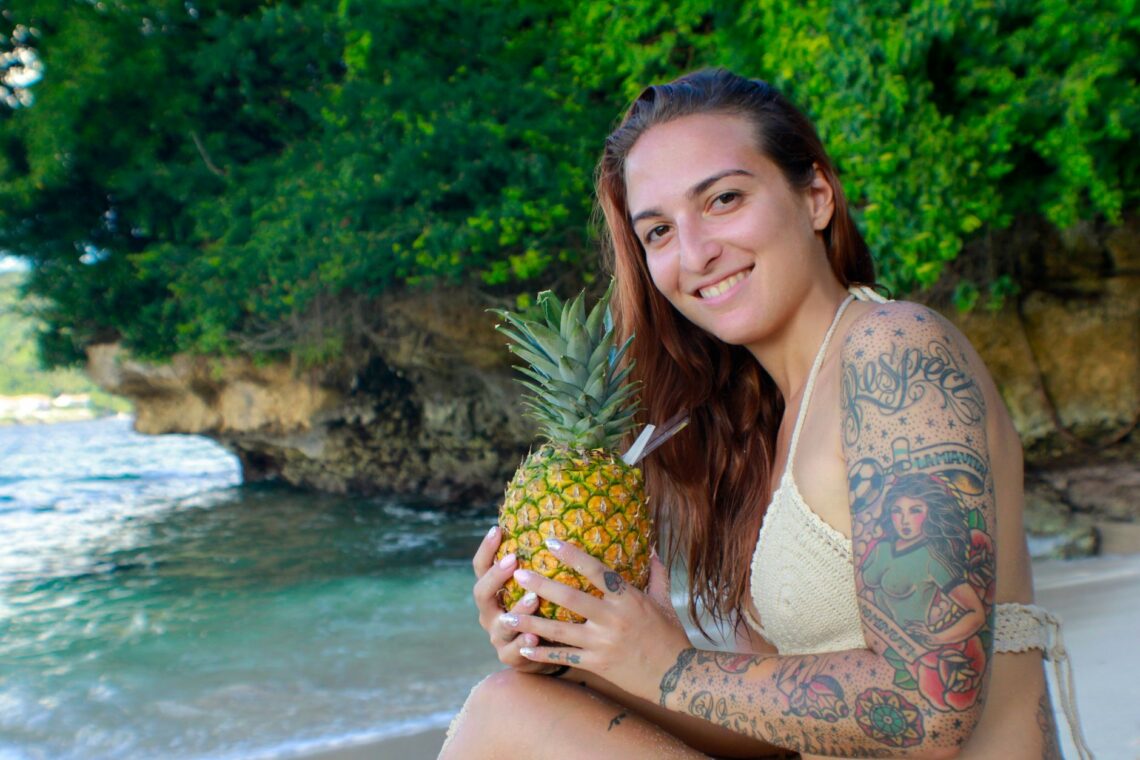 tattooed woman holding pineapple on tropical beach