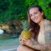 tattooed woman holding pineapple on tropical beach
